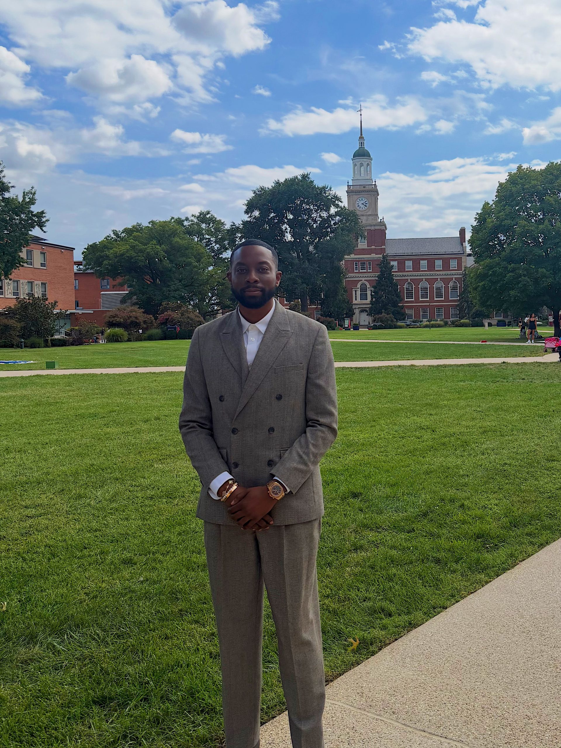 John Imah standing on Howard University’s campus with the lawn and clock tower behind him.